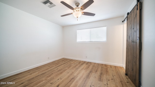 spare room featuring ceiling fan, a barn door, and light wood-type flooring