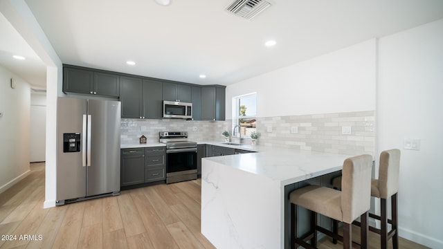 kitchen with light stone counters, light hardwood / wood-style flooring, kitchen peninsula, gray cabinets, and appliances with stainless steel finishes