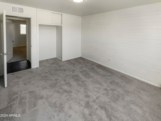 unfurnished bedroom featuring light carpet, a closet, and brick wall