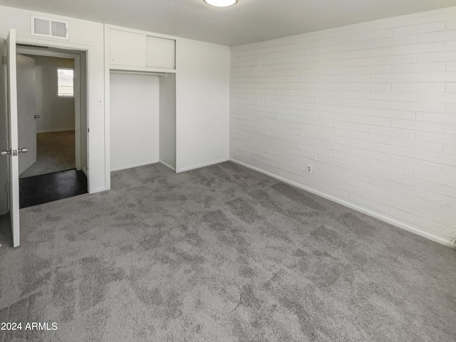 unfurnished bedroom featuring a closet, brick wall, carpet, baseboards, and visible vents