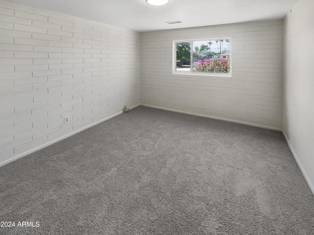 carpeted empty room featuring brick wall and baseboards