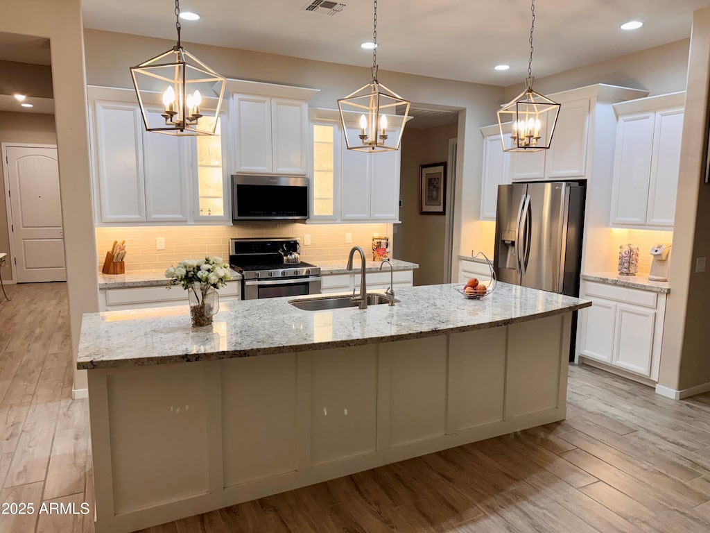 kitchen featuring a kitchen island with sink, a sink, backsplash, stainless steel appliances, and light wood-style floors