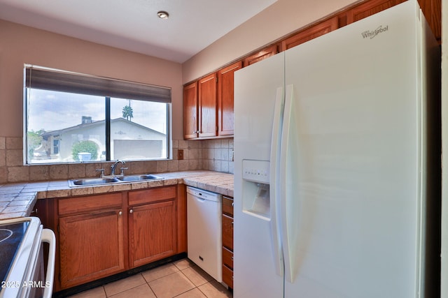 kitchen with light tile patterned flooring, a sink, white appliances, brown cabinetry, and backsplash