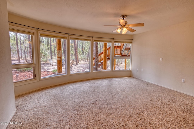 carpeted spare room with a wealth of natural light, a ceiling fan, and baseboards