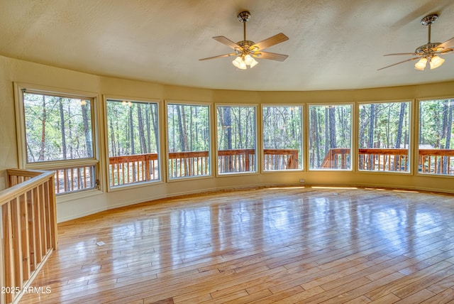 unfurnished sunroom with hardwood / wood-style floors, baseboards, plenty of natural light, and a textured ceiling