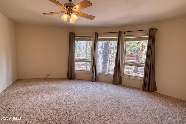 carpeted spare room with ceiling fan, baseboards, and a wealth of natural light