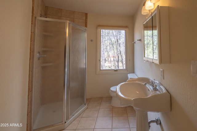 bathroom featuring baseboards, a sink, toilet, tile patterned floors, and a stall shower