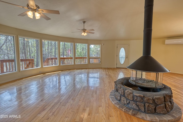 living area with a wood stove, a wall unit AC, a ceiling fan, light wood finished floors, and baseboards