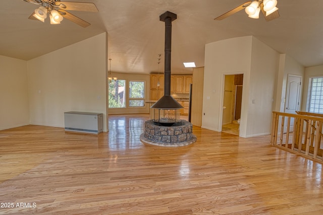unfurnished living room featuring light wood-type flooring, a wood stove, a ceiling fan, and lofted ceiling