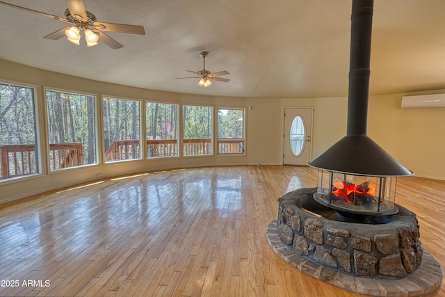 living area featuring a wood stove, a ceiling fan, a wall mounted AC, and light wood finished floors