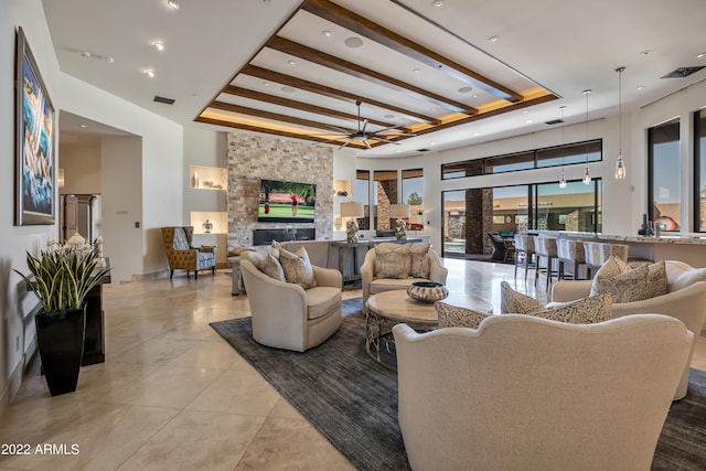 tiled living room with beam ceiling, a raised ceiling, and a stone fireplace