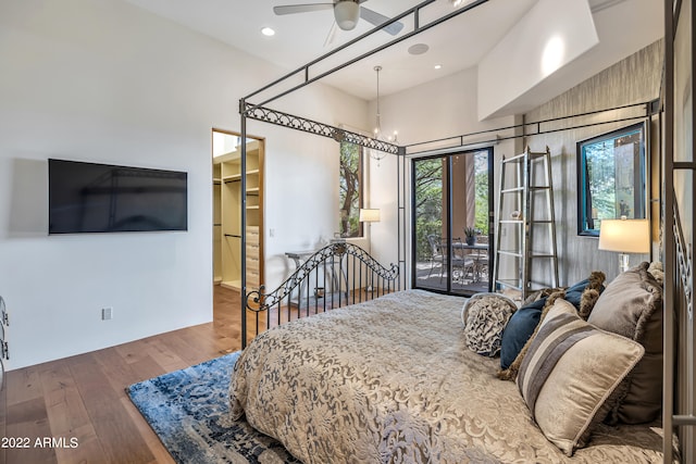 bedroom with a walk in closet, access to exterior, ceiling fan with notable chandelier, a towering ceiling, and dark hardwood / wood-style flooring