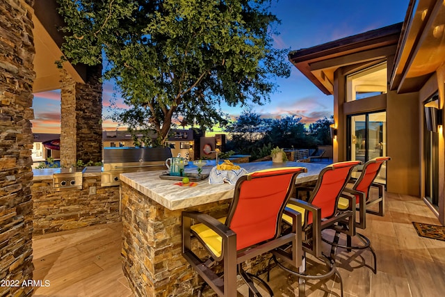 patio terrace at dusk with exterior bar, grilling area, and an outdoor kitchen