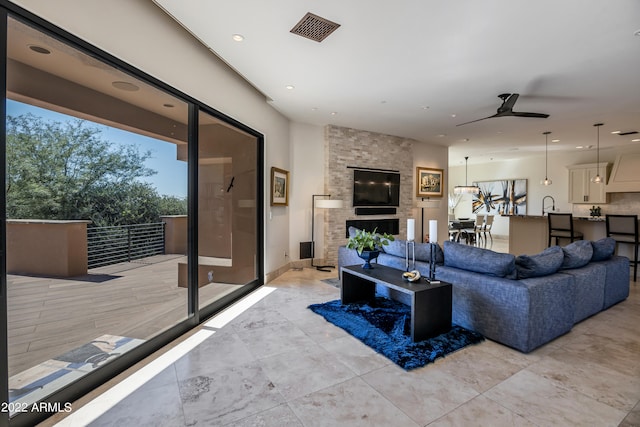 tiled living room with a large fireplace, ceiling fan, sink, and a wealth of natural light