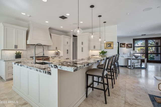 kitchen with an island with sink, hanging light fixtures, white cabinets, and light stone countertops