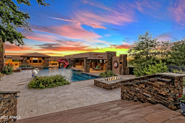 pool at dusk featuring a water slide and a patio