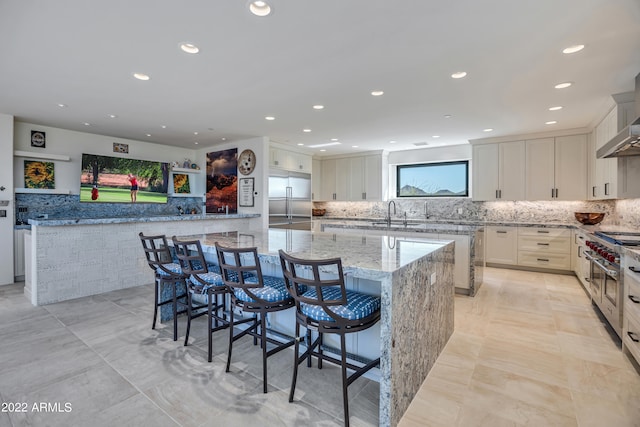 kitchen featuring light stone counters, a kitchen island, a breakfast bar area, high quality appliances, and white cabinetry