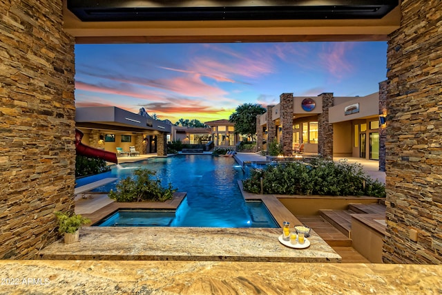 pool at dusk featuring a patio, a hot tub, and a water slide