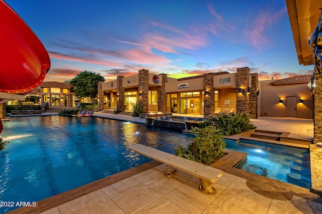 pool at dusk with a patio, a diving board, an in ground hot tub, and french doors