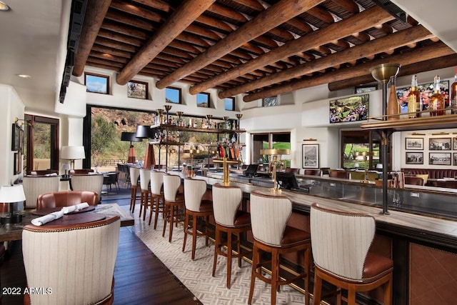 bar featuring dark wood-type flooring, beamed ceiling, and stainless steel counters