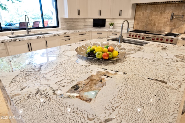 kitchen with range, light stone counters, tasteful backsplash, white cabinets, and sink