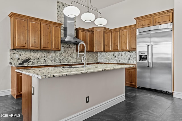 kitchen featuring sink, light stone countertops, a center island with sink, built in fridge, and wall chimney exhaust hood