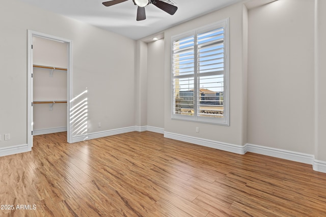 unfurnished bedroom with ceiling fan, a walk in closet, a closet, and light wood-type flooring