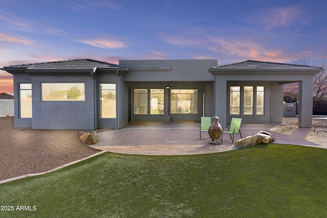 back house at dusk featuring a lawn and a patio