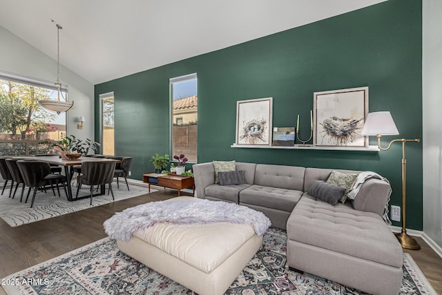 living area with an accent wall, vaulted ceiling, wood finished floors, and baseboards