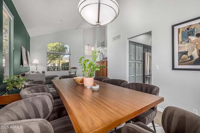 dining room featuring visible vents, high vaulted ceiling, and wood finished floors