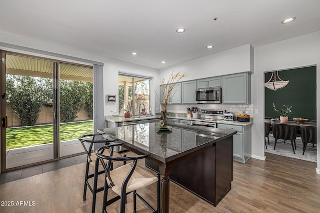 kitchen with dark stone counters, decorative backsplash, gray cabinets, appliances with stainless steel finishes, and dark wood-style flooring