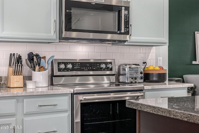 kitchen with white cabinetry, backsplash, stone countertops, and appliances with stainless steel finishes