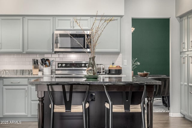 kitchen with gray cabinets, backsplash, dark wood finished floors, stainless steel appliances, and stone counters
