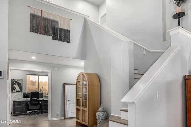stairway with recessed lighting, baseboards, a high ceiling, and wood finished floors