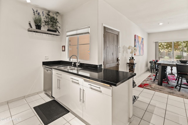 kitchen featuring stainless steel dishwasher, dark countertops, light tile patterned flooring, and a sink