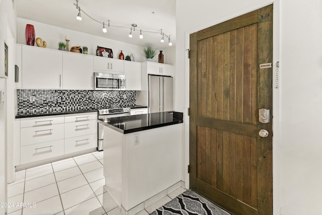 kitchen with dark countertops, backsplash, light tile patterned floors, appliances with stainless steel finishes, and white cabinets