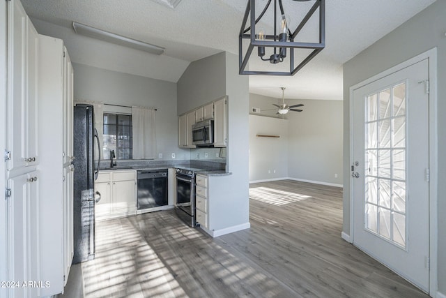 kitchen with ceiling fan with notable chandelier, vaulted ceiling, black appliances, decorative light fixtures, and white cabinets