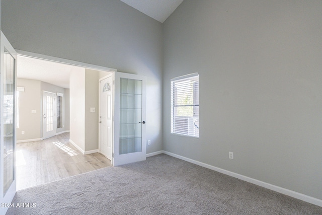 carpeted spare room featuring french doors and high vaulted ceiling