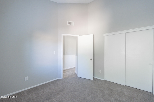 unfurnished bedroom featuring light carpet, a high ceiling, and a closet