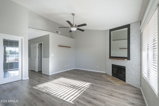 unfurnished living room with ceiling fan, a stone fireplace, a textured ceiling, lofted ceiling, and light wood-type flooring