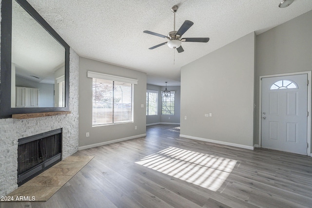 unfurnished living room featuring lofted ceiling, ceiling fan, a textured ceiling, a fireplace, and wood-type flooring