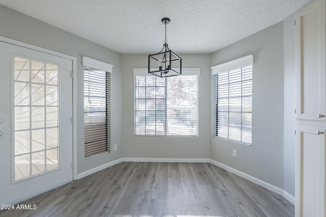 unfurnished dining area with a textured ceiling, light hardwood / wood-style floors, an inviting chandelier, and plenty of natural light