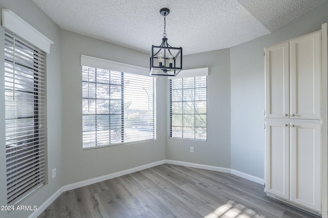 unfurnished dining area with a textured ceiling, light hardwood / wood-style flooring, and an inviting chandelier