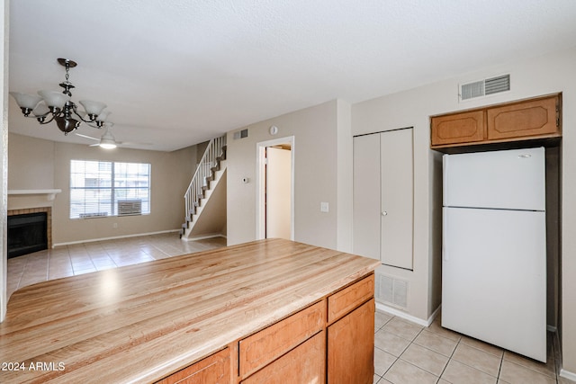 kitchen featuring white refrigerator, light tile patterned flooring, a tiled fireplace, decorative light fixtures, and a chandelier