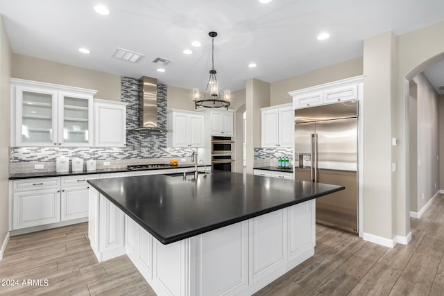 kitchen with decorative light fixtures, wall chimney exhaust hood, a chandelier, appliances with stainless steel finishes, and light wood-type flooring