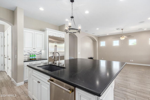 kitchen with white cabinets, sink, a kitchen island with sink, appliances with stainless steel finishes, and ceiling fan with notable chandelier