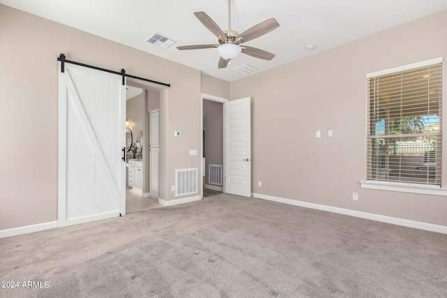 unfurnished bedroom with connected bathroom, ceiling fan, carpet flooring, and a barn door