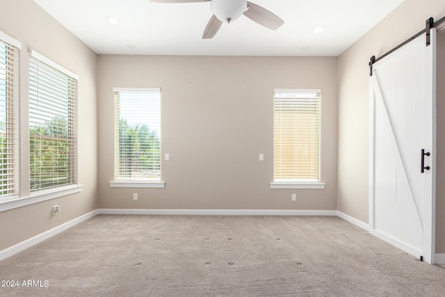 carpeted spare room with a barn door and ceiling fan