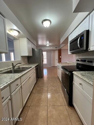 kitchen with light tile patterned floors, sink, light stone countertops, appliances with stainless steel finishes, and white cabinets