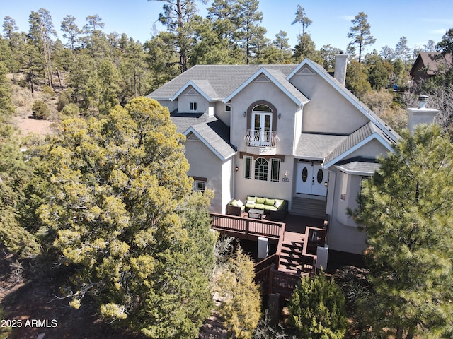 exterior space with a balcony, a shingled roof, a chimney, stucco siding, and french doors